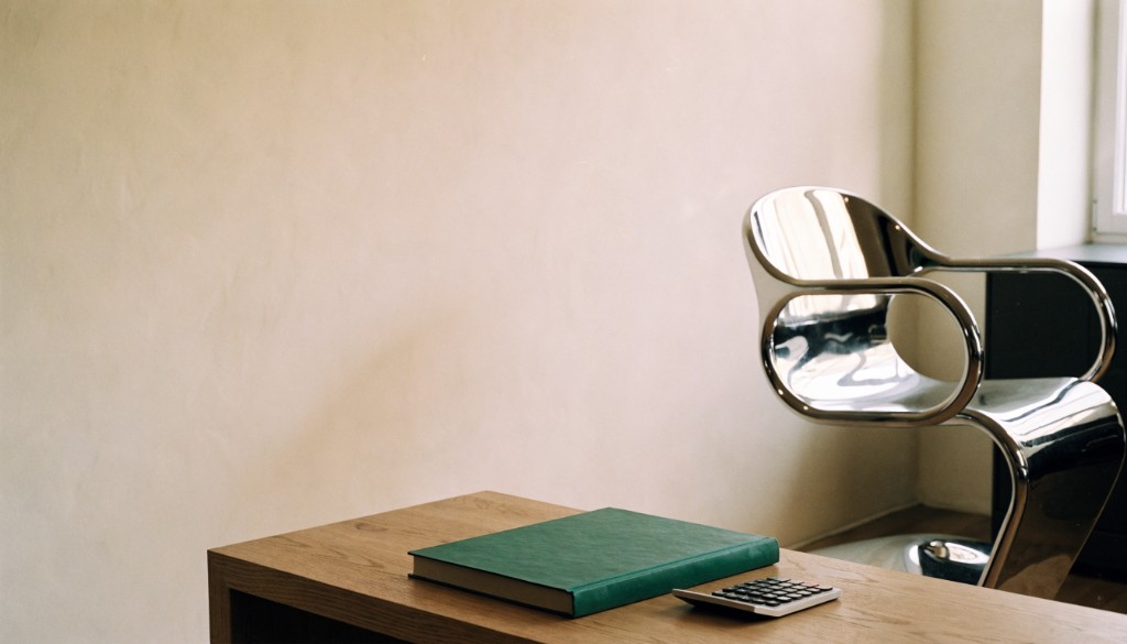 Chrome salon chair beside an oak desk with a green ledger and calculator.