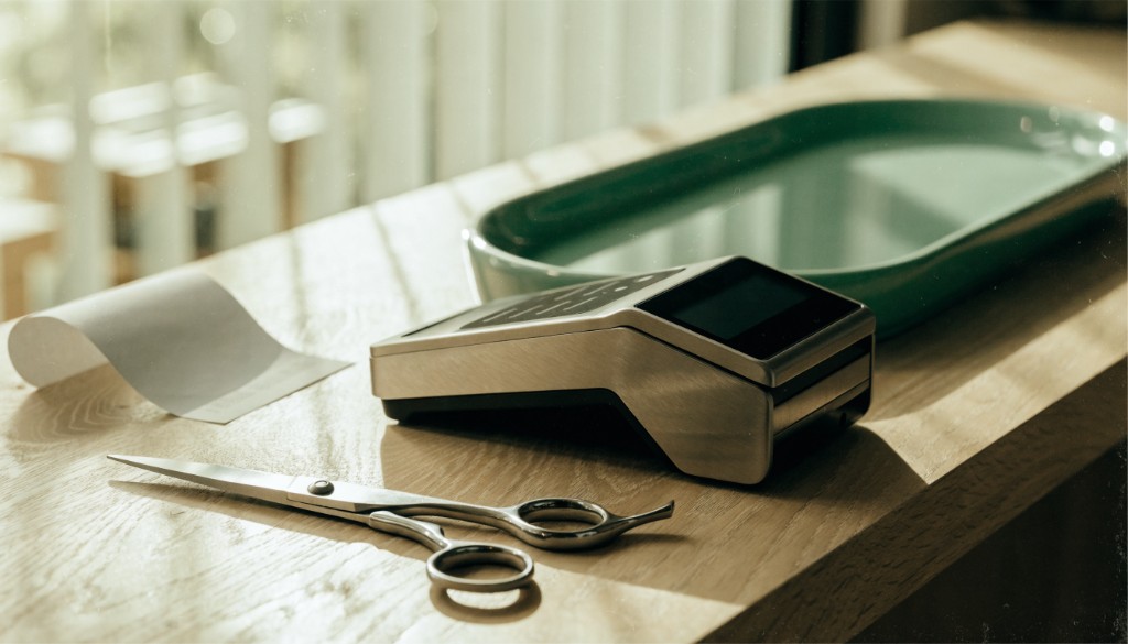 Unbranded payment terminal beside scissors and a blank receipt on an oak counter.